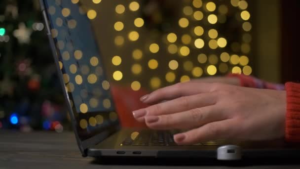 Online einkaufen. Frau kauft Geschenke für Weihnachten und Neujahr mit Laptop und Kreditkarte. Gemütliches Café oder Zuhause. Hintergrund Weihnachtsbeleuchtung. — Stockvideo