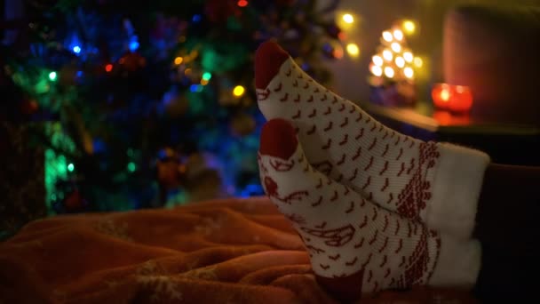 Close-up de um par de pernas em meias de Natal ao lado de uma árvore de Natal. — Vídeo de Stock