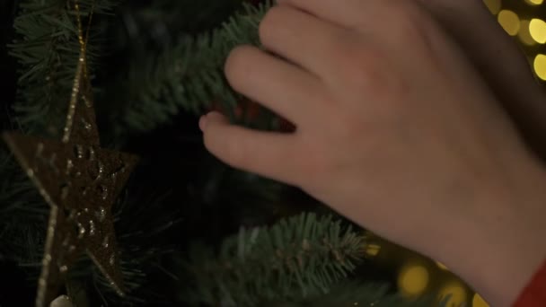 Close-up of woman hands decorating Christmas tree with balls on the background of bright festive lights. — Vídeo de stock