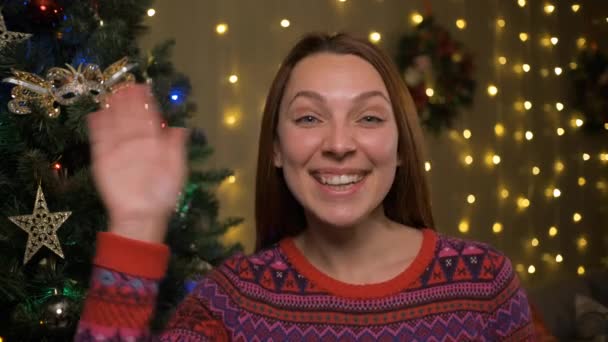 X-masを作る女性は、リモートで親戚の家族を祝うビデオ会議を前に、輝く光の近くの家に座ってクリスマスツリー、現代的な技術コンセプト — ストック動画