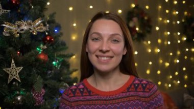 Gülümseyen kadın arka planda mutlu Noeller, Noel ağacı ve dekore edilmiş bir oda diliyor.