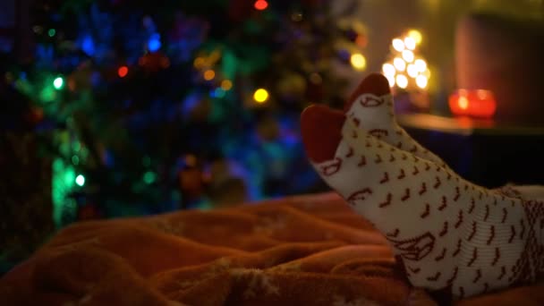 Nahaufnahme eines Beinpaares in Weihnachtssocken neben einem Weihnachtsbaum. Konzept des Wartens auf Weihnachten. — Stockvideo