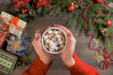 Bir kadın elinde lokumlu sıcak bir fincan kakao tutuyor. Noel süsleri, hediyeler ve ahşap arka plan. Yüksek kalite fotoğraf
