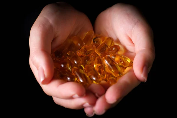 Sarı kapsül D vitamini, E vitamini, Omega-3 kadın eli yakın plan, siyah arka plan. Bakım, sağlık, sağlıklı beslenme