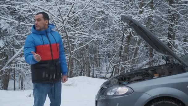 Homme debout sur la route près de la voiture cassée et essayant d'attraper de l'aide sur la route forestière d'hiver — Video