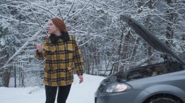 Kış ormanında genç bir kadın yolda kırık bir arabayla duruyor, arabaları durduruyor, yardım bekliyor.