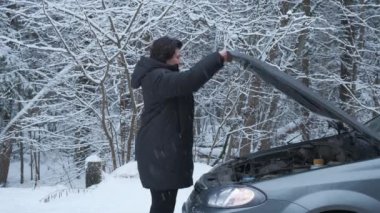 Kadın motoru kontrol etmek için bozuk arabanın kaputunu açıyor.