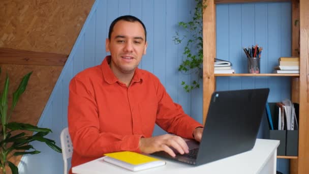 Portret szczęśliwego młodego biznesmena, siedzącego przy stole w biurze i pracującego na laptopie. Portret wesołego ucznia, studiującego na laptopie w domu. uśmiecha się i wygląda w aparacie. — Wideo stockowe