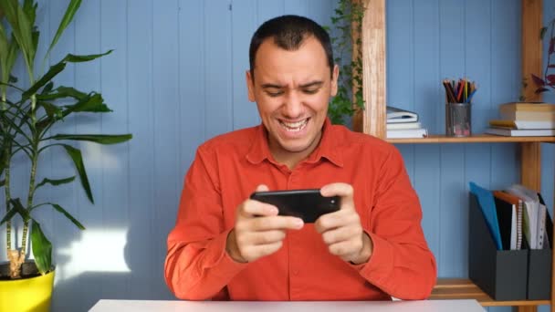 Hombre feliz está jugando videojuego en la oficina del hogar con un teléfono inteligente moderno — Vídeo de stock