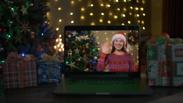 Χαμογελαστή γυναίκα με καπέλο santa σε ένα videocall, είναι ευτυχισμένη και εύχεται Καλά Χριστούγεννα σε απευθείας σύνδεση, χριστουγεννιάτικο δέντρο και διακοσμημένο εσωτερικό δωμάτιο στο παρασκήνιο — Αρχείο Βίντεο