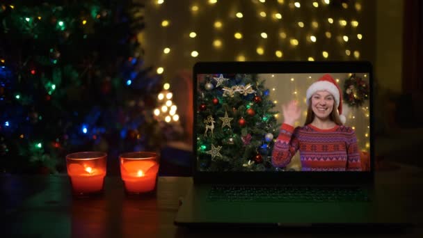 Usmívající se žena se Santa klobouk na videokalonu, ona je šťastná a přeje veselé Vánoce on-line, vánoční stromeček a zdobené interiér místnosti v pozadí — Stock video