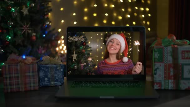 Šťastná žena s jiskry a Santa klobouk blahopřeje příbuzným k Vánocům přes notebook on-line. — Stock video