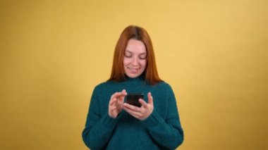 Stüdyoda sarı arka planda izole bir şekilde poz veren gülümseyen genç bir kadın. Cep telefonu kullanırken şaşırmış görün. İnsanlar samimi duygular yaşam tarzı konsepti.