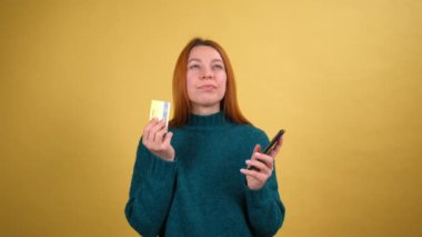 Cep telefonu kullanan genç bir kadın kredi kartı kullanıyor ve harika bir fikri var. Evet de. sarı arkaplan stüdyosunda izole.