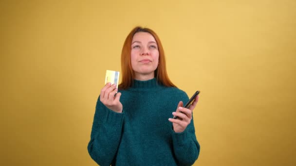 使用手机的年轻妇女持有有伟大新想法的银行卡说是的。隔离在黄色背景工作室. — 图库视频影像