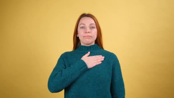 Uczciwa, odpowiedzialna młoda kobieta podnosząca rękę, dotykająca klatki piersiowej i składająca przysięgę, obiecująca, patrząca przed kamerą godna zaufania. kryty izolowany na żółtym tle — Wideo stockowe