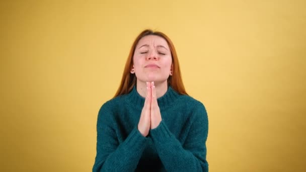 Mujer joven molesta apelando a la cámara con ruegos suplicando ojos, manteniendo el gesto de oración y pidiendo ayuda. estudio de interior tiro aislado sobre fondo amarillo — Vídeos de Stock