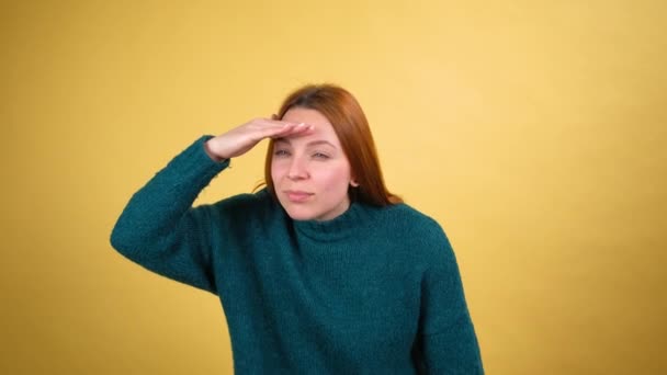 Nieuwsgierige jonge vrouw die hand in hand kijkt en ver weg kijkt met aandachtige blik, ambitieuze studentenplannen maakt voor de toekomst, perspectieven bekijkt. indoor studio shot gele achtergrond — Stockvideo