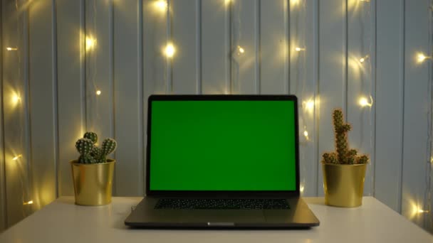 Ordenador portátil de pantalla verde en un escritorio de tareas en habitación oscura con fondo de guirnalda — Vídeos de Stock