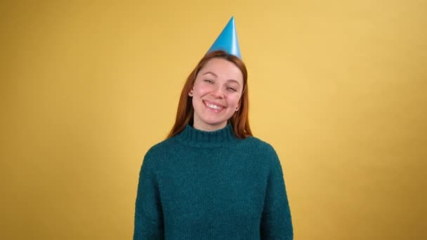 Optimista mujer joven encantada con cono divertido en su cabeza soplando cuerno de fiesta, celebrando cumpleaños felicitando en aniversario, estado de ánimo festivo. — Vídeos de Stock