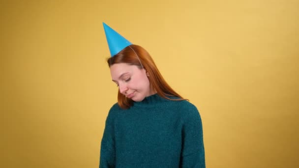 Smutna młoda kobieta ze śmiesznym rożkiem na głowie świętuje urodziny samotnie. Kryty studio strzał izolowany na żółtym tle. — Wideo stockowe