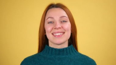 Çekici kızıl saçlı kadının yakından çekilmiş portresi kameraya bakan dişlek gülüşlü, pozitif mutlu duygularla. Stüdyo çekimi sarı arkaplanda izole edildi