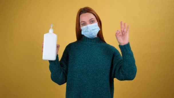 Молода жінка в медичній масці тримає пляшку з антибактеріальним гелем, жестикулює великі пальці вгору, рекомендуючи відмінний антисептичний, дезінфікуючий захист від інфекції, коронавірус . — стокове відео