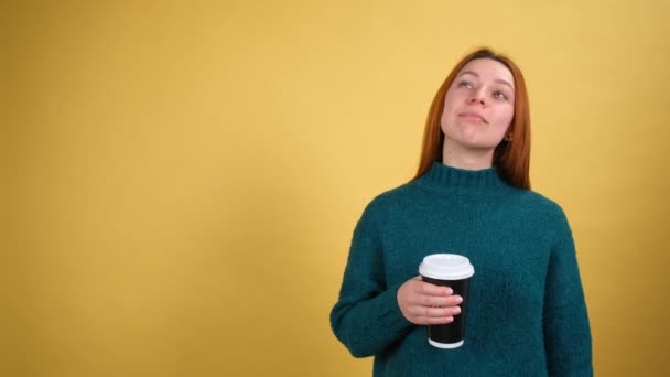 Спокойные красивые рыжие волосы молодая женщина в зеленом свитере Держите чашку кофе, пить, наслаждаться. Пепе изолирован на желтом фоне в студии. Люди искренние эмоции, образ жизни концепции. — стоковое видео