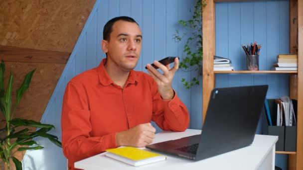 Hombre joven grabando mensaje de voz en el teléfono inteligente en la oficina en casa — Vídeos de Stock