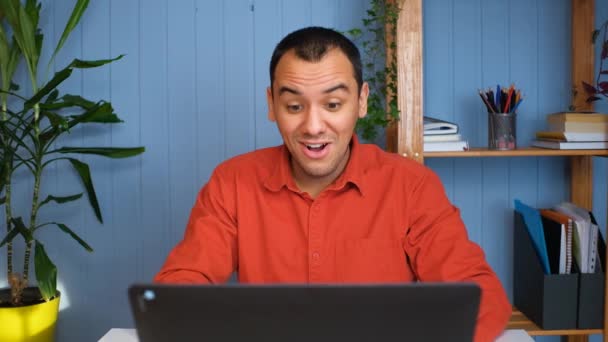 A fiatal üzletember sikeres híreket kap, otthon ül az asztalnál laptoppal. — Stock videók