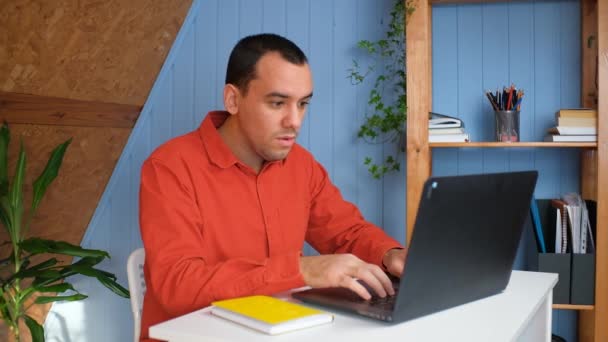 Young business man gets successful news, sits at table with laptop in home office. — Stock Video