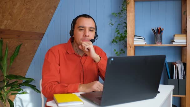 ヘッドフォンの悲しい男は、ノートパソコンの思考の前に机に座って、困難を持っている、検索の問題解決策 — ストック動画