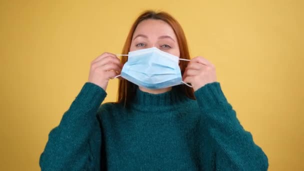 Young woman with face hygienic medical mask to prevent respiratory infection, contagious coronavirus. indoor studio shot isolated on yellow background — Stock Video