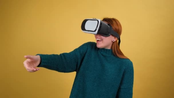 Молодая женщина с помощью шлема гарнитуры VR app. жест слайда. изолированные на желтом фоне в студии — стоковое видео