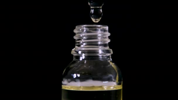 El aceite cosmético gotea de una pipeta en una botella de vidrio sobre un fondo negro. Goteo de aceite de un gotero. — Vídeo de stock
