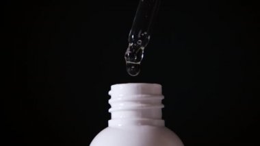 Tıbbî bir şişedeki pipetten düşüş, siyah bir arka planda izole edilmiş, yakın plan.