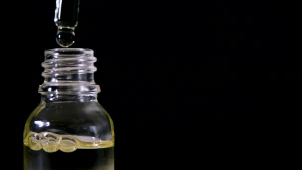 Droppa olja från pipett i glasflaska på svart bakgrund. — Stockvideo