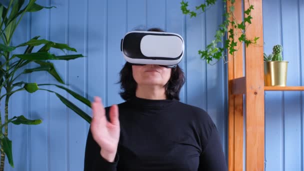 Uma mulher idosa usa óculos de realidade virtual. O futuro quotidiano da casa. Pessoas idosas e conceito de tecnologia moderna — Vídeo de Stock