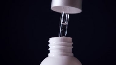 A mans hand takes a dropper dropper bottle with serum, lifts it up and makes a few drops in a bottle. close-up
