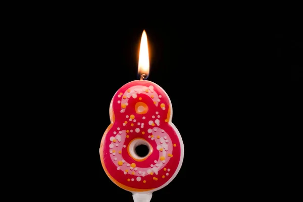8 numaralı doğum günü pastası. Pembe donut mumları daha hafif, siyah arka planda yanıyor.