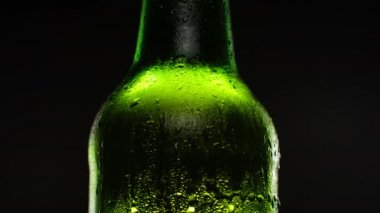 Su damlalarıyla kaplı bira şişesi koyu arkaplanda dönüyor..