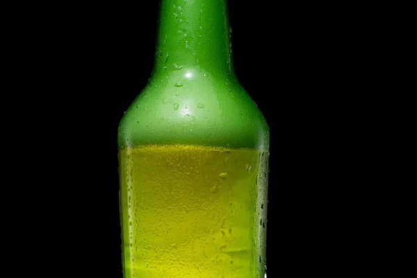 Siyah arka planda köpüklü yeşil bira şişesi..