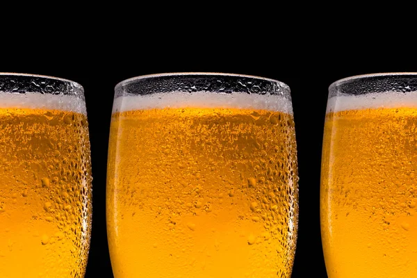 A row of beer glasses with beer on a black background. Space for text and logo. Drops of water trickle down the glass. — Stock Photo, Image