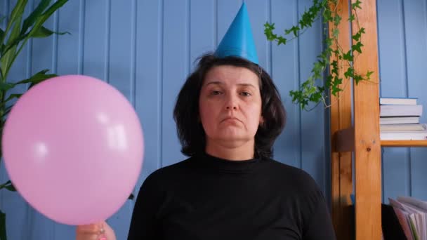 Een eenzame ongelukkige, droevige oude vrouw met pet die naar de camera kijkt en ballonnen vasthoudt, die alleen haar verjaardag viert. — Stockvideo