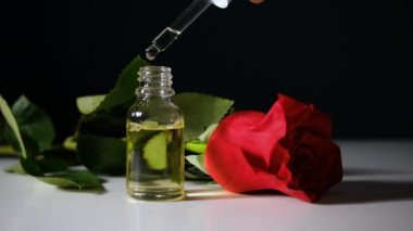 Pipetten cam şişeye yağ damlatıyor. Rose arka planda. Doğal Cilt Yağı