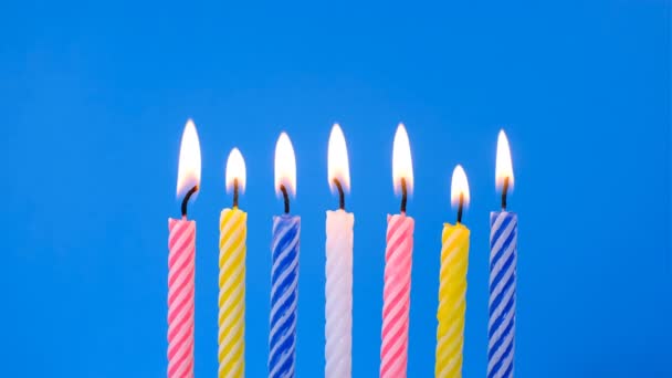 Velas de cumpleaños sobre un fondo azul. La vela es de color amarillo, rosa, azul y blanco — Vídeo de stock