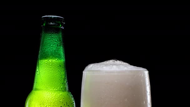 Un vaso de cerveza con espuma junto a una botella de cerveza verde. Cerveza fría y refrescante. — Vídeo de stock