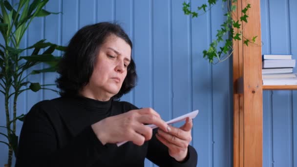 Жінка середнього віку, сидячи вдома, читає погані новини . — стокове відео
