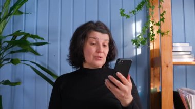 Zafer konsepti. Neşeli son sınıf öğrencisi kadın akıllı telefon ekranına bakar ve aşırı sevinç hisseder, piyangoyu kazanır, iyi haberler alır. Evde zafer kazanmış olgun bir bayan.