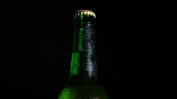 Uma garrafa de cerveja gelada no escuro é iluminada pela luz. Luz fria e cerveja refrescante. — Vídeo de Stock